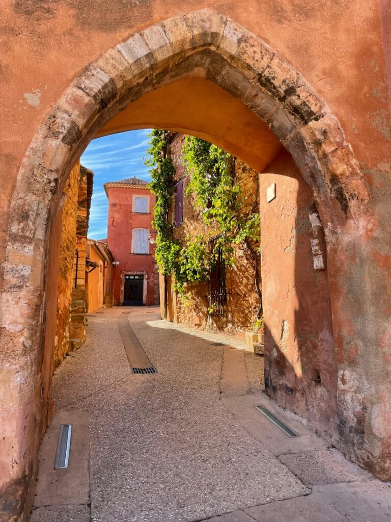 Charming archway leading to rustic street in Roussillon, France, highlighting vibrant architecture.